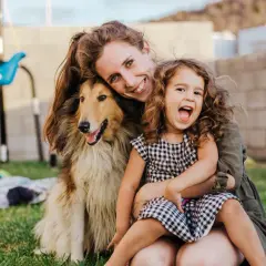 Uśmiechnięta rodzina: mama, córka i pies dla dzieci, cieszą się wspólnym popołudniem na trawniku.