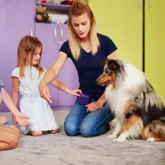 Dzieci i pies uczestniczą w sesji dogoterapii. Kobieta instruuje psa, a dzieci z uwagą obserwują.