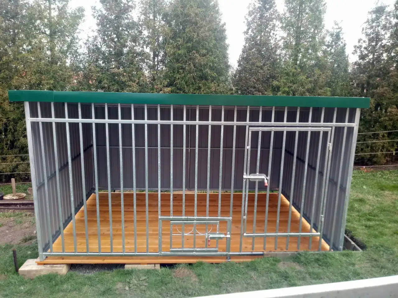 Nowoczesna buda z metalowymi prętami i drewnianą podłogą. Czy pies może być na łańcuchu? Ta buda daje mu przestrzeń.